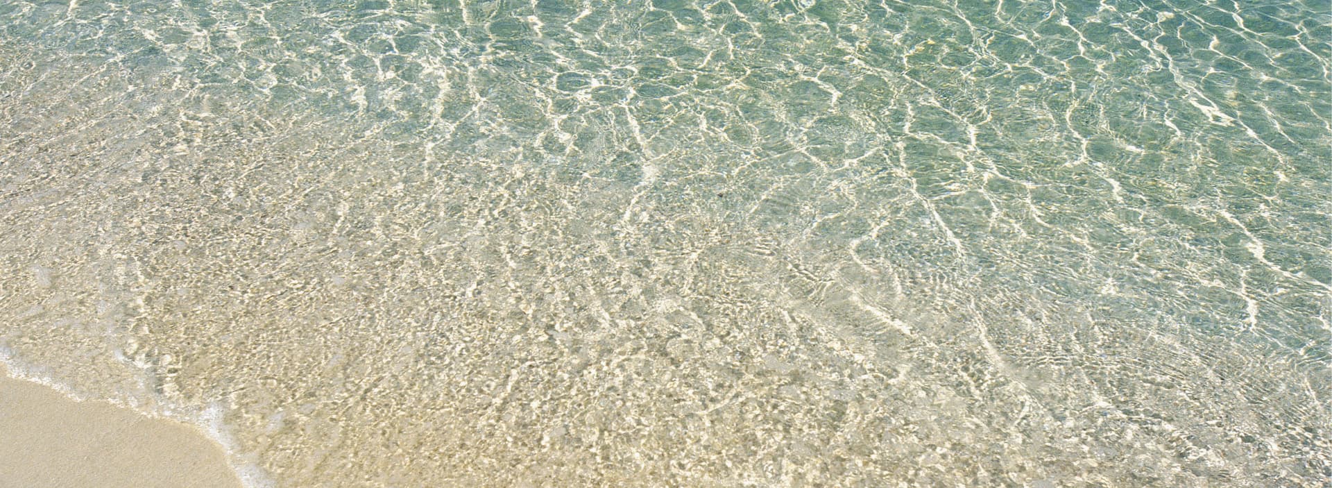 Clear turquoise water gently rippling over a sandy beach.