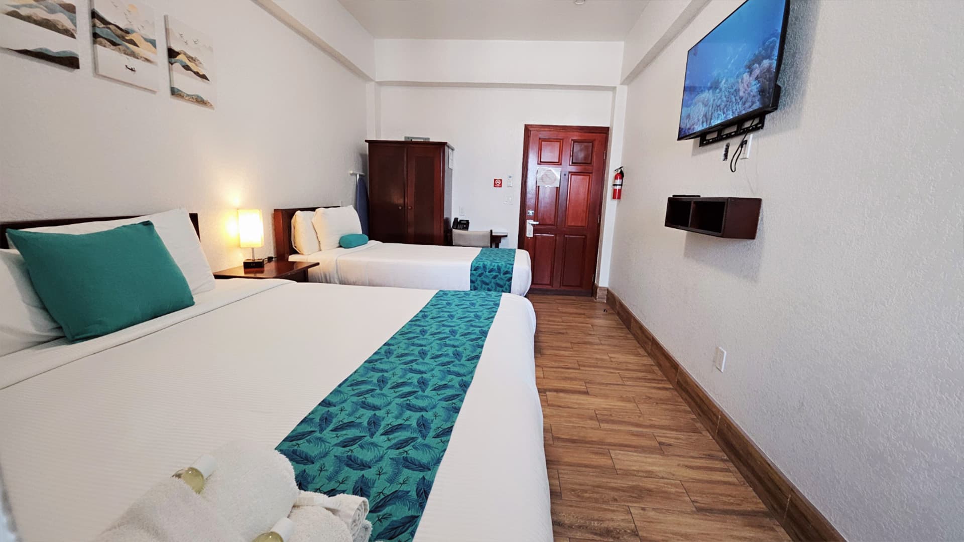 A cozy hotel room featuring two beds, a TV, and decorative artwork.