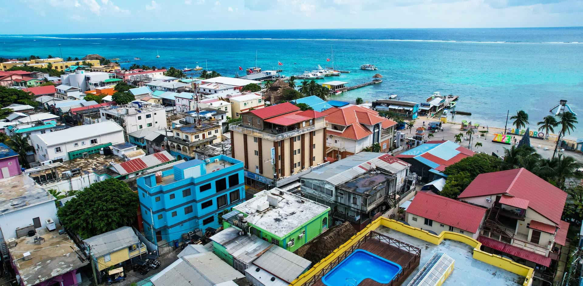 Aerial view of colorful buildings and a harbor along a turquoise coastline.